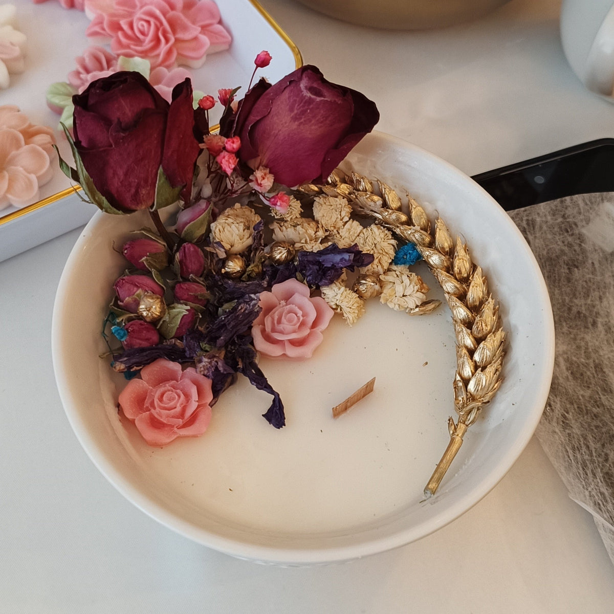 Bougie fleurie aux roses séchées, blés dorés et roses en cire dans un bol blanc